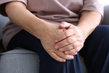 Elderly woman suffering from pain in knee at home, closeup