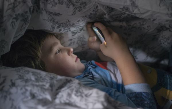 Barn med telefon i sengen