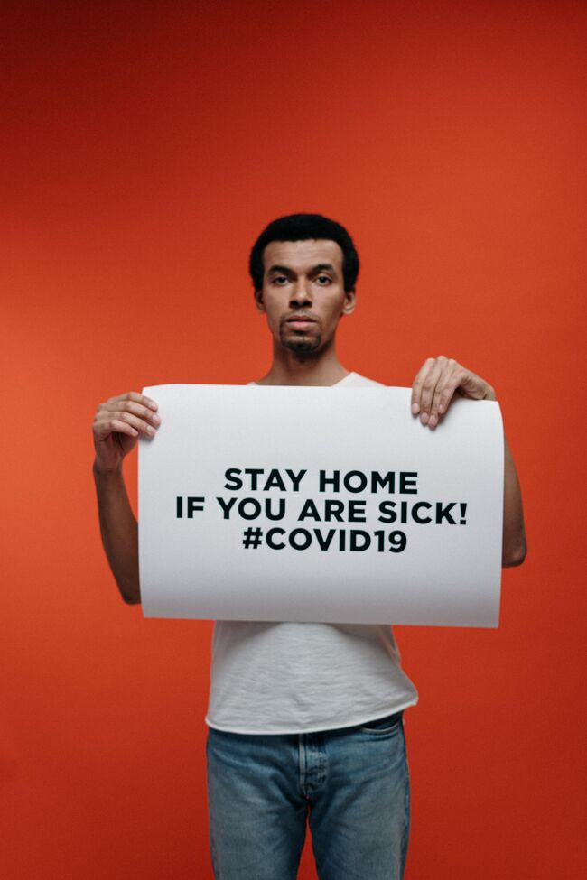 Bildet viser en mann som holder en plakat om å holde deg hjemme dersom du er syk av Covid-19.