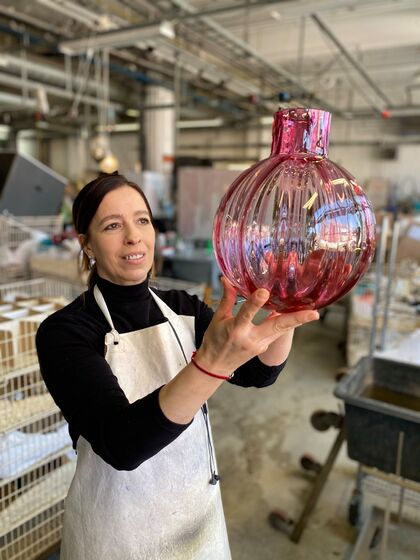 Bildet viser ei som holder opp en stor glasskuppel, lampe, blåst på Hadeland Glassverk