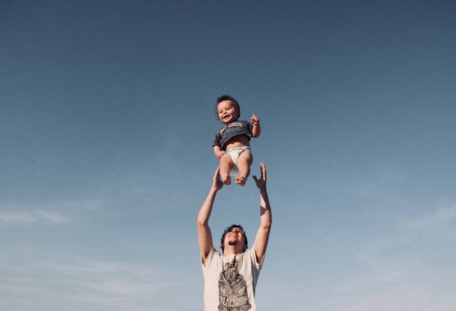 Bildet viser en far som kaster barnet sitt opp i lufta.