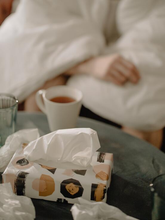Bildet viser et bord med papirlommetørkler, te kopp og tydelig at en er syk.