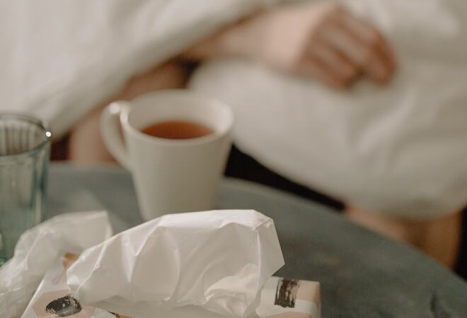 Bildet viser et bord med papirlommetørkler, te kopp og tydelig at en er syk.