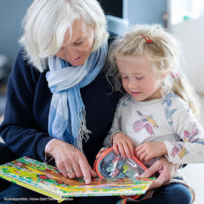 Frivillig eldre dame leser i bok sammen med jente.