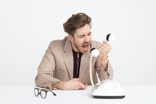 Bildet viser en frustrert mann som roper inn i telefonrøret