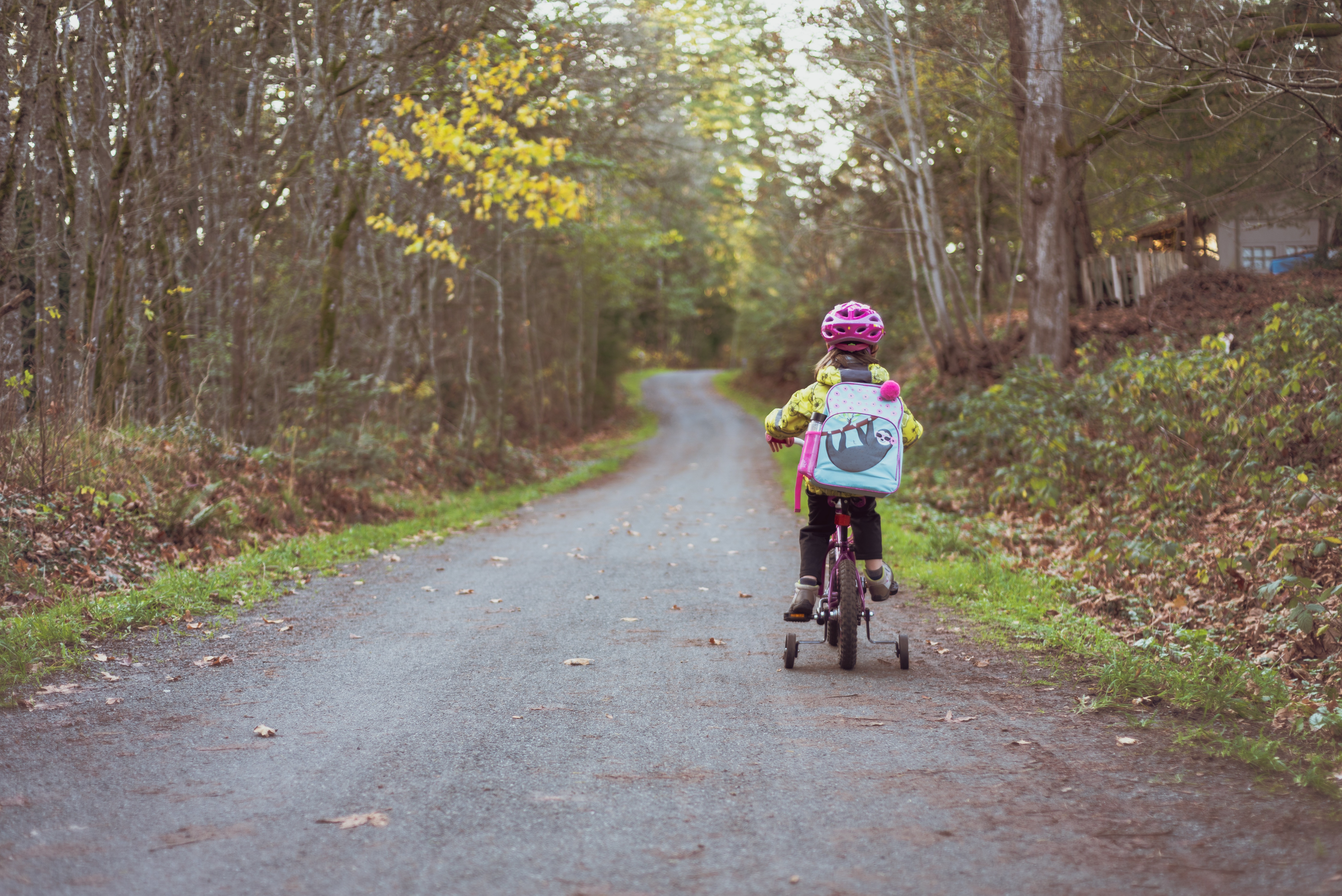 Bilde av et barn som sykler med ryggsekk gjennom skogen på grusvei