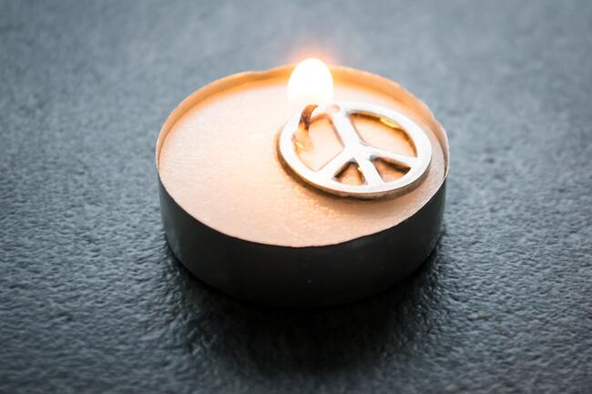 Bildet viser et peace-symbol og et stearinlys som lyser.