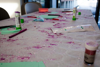 Store mengder lilla glitter på et bord. Man ser også limstifter og tusjer.