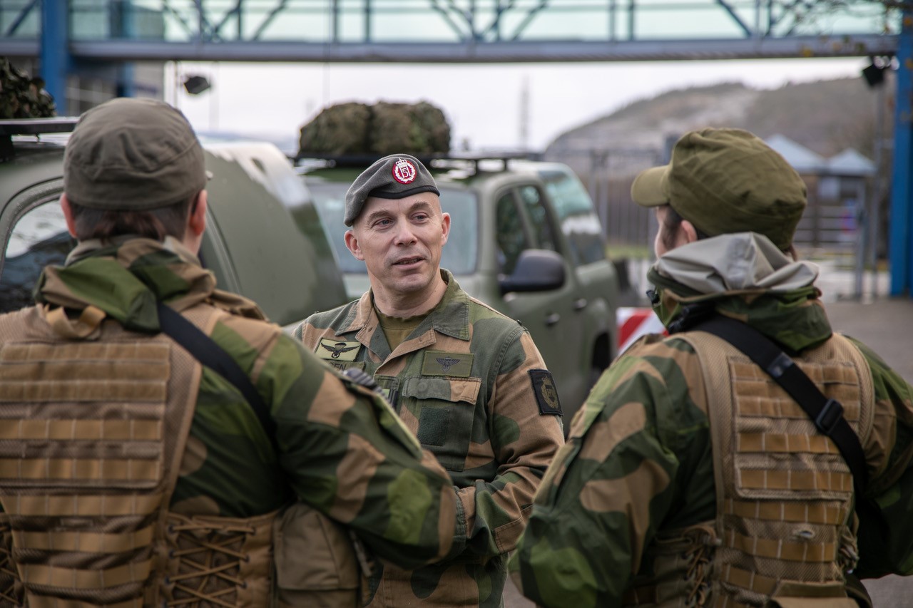 Bildet viser tre personer kledd i militæruniform foran militærkjøretøy. De prater sammen. Foto: Tore Ellingsen