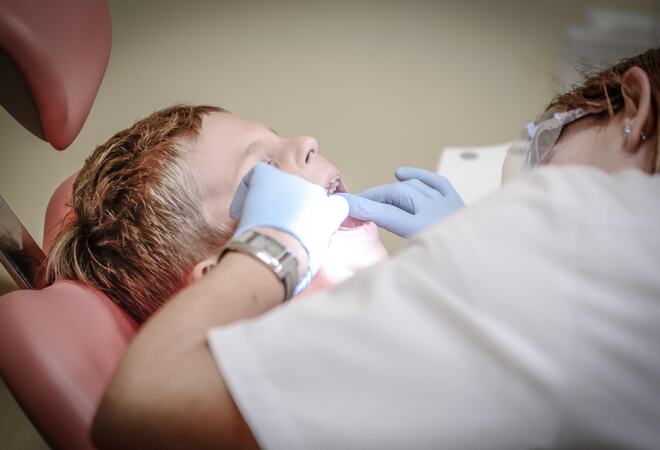Bildet viser et bart som ligger i en tannlegestol med gapende munn, mens en tannlege jobber.