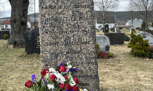 Bildet viser en gravstein med blomsterkrans foran.
