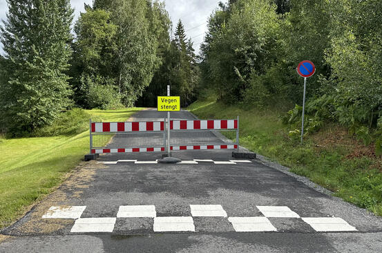 Bildet viser en vei som er stengt med sperring og skilt.