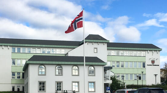 Hvitt bygg med Fauske kommune logo og norsk flagg i forgrunn.