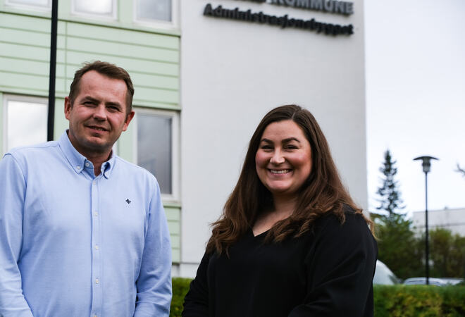 En mann og en kvinne smiler. De står foran et bygg
