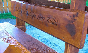 Rygg på en benk i tre med skriften En gave til bygda fra 2007-kullet
