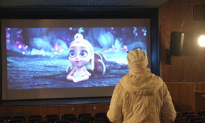 Kvinne står med ryggen til i kinosalen og ser film på lerettet