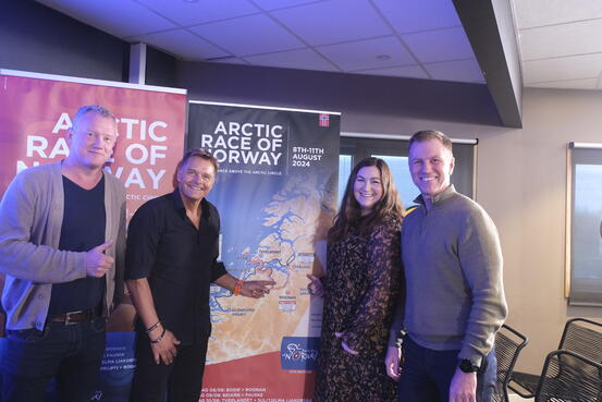 Tre menn og en kvinne peker på en roll-up med etappene i Arctic Race og Norway