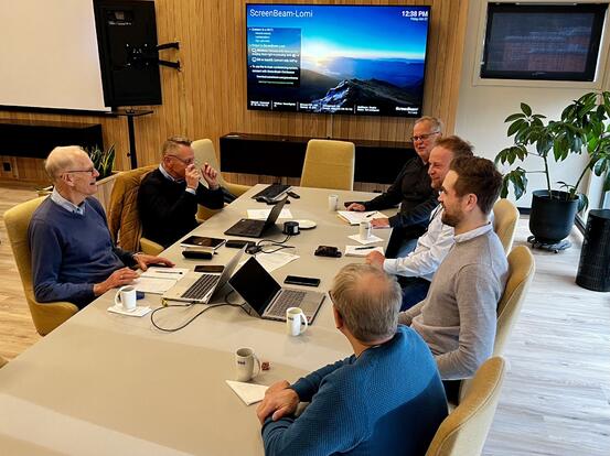 seks menn rundt et møtebord med pcer og TV i bakgrunn