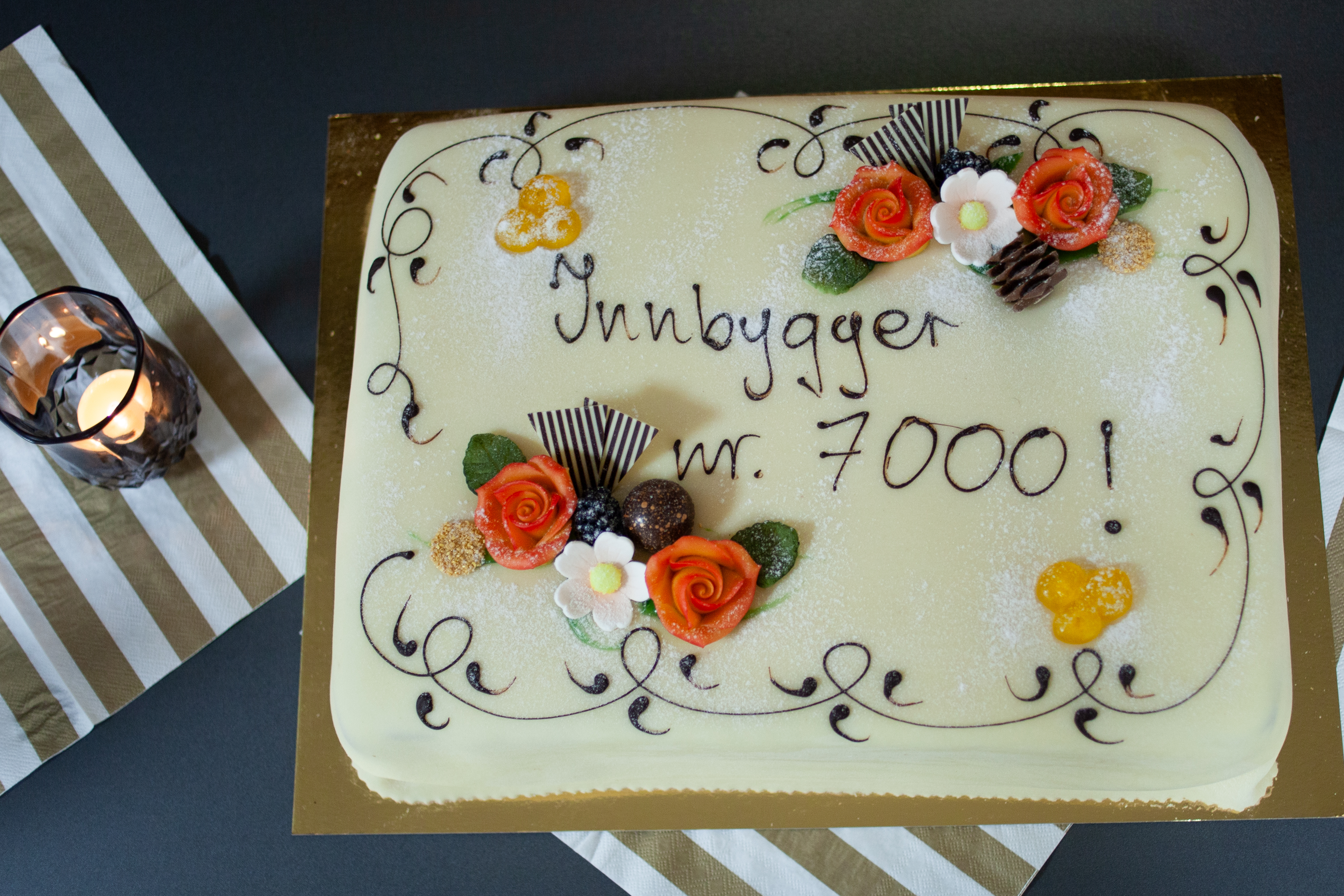 Bildet viser en kake. Den er dekorert med blant annet orange og hvite blomster. Over to linjer står teksten 