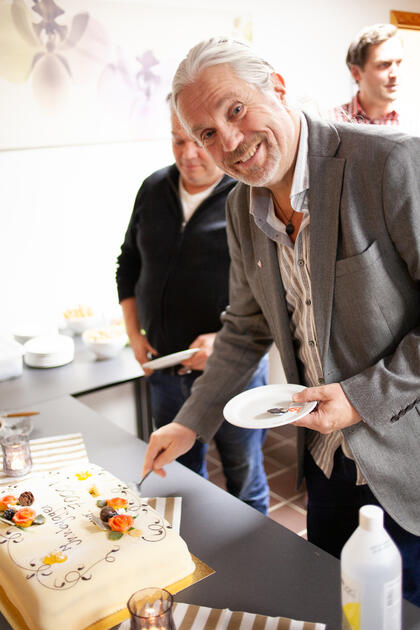 Bildet viser en mann som er i ferd med å ta det første stykket av kaken. Kakespaden er på kaken. Han smiler bredt.