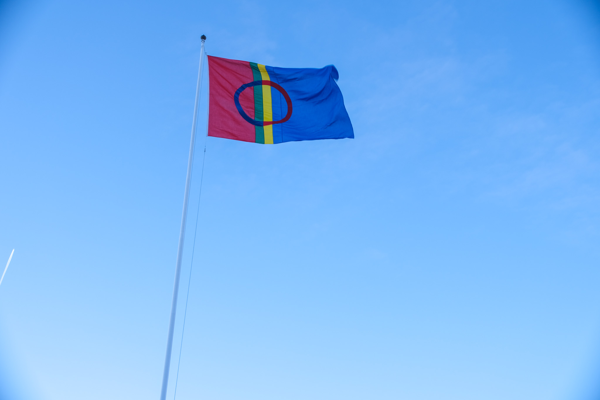 Samisk flagg i toppen av flaggstang. Blå himmel i bakgrunn