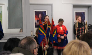 Små håndholdte samiske flagg står i en vase. Mennesker på konsert i forgrunn. Artistene for kvelden i bakgrunn