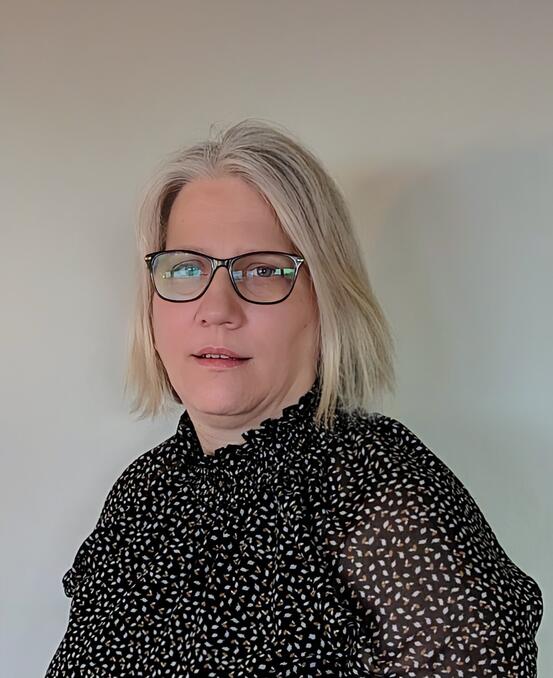 Portrett av voksen kvinne med kort blondt hår og svart bluse med hvite prikker.