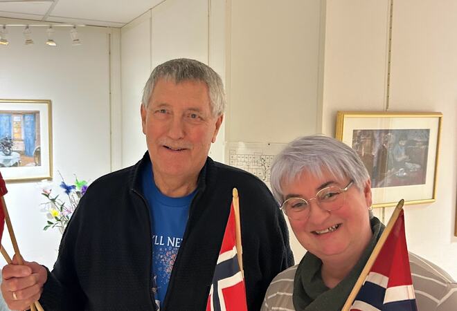 En mann og en kvinne smiler. De holder begge håndholdte norske flagg