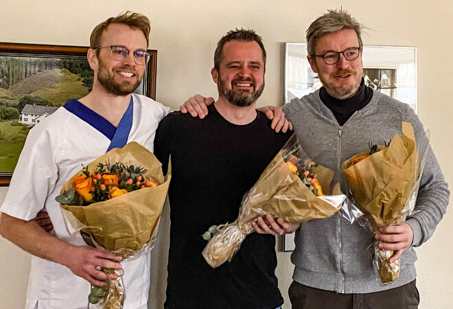 Tre menn holder hver sin blomsebukett og smiler