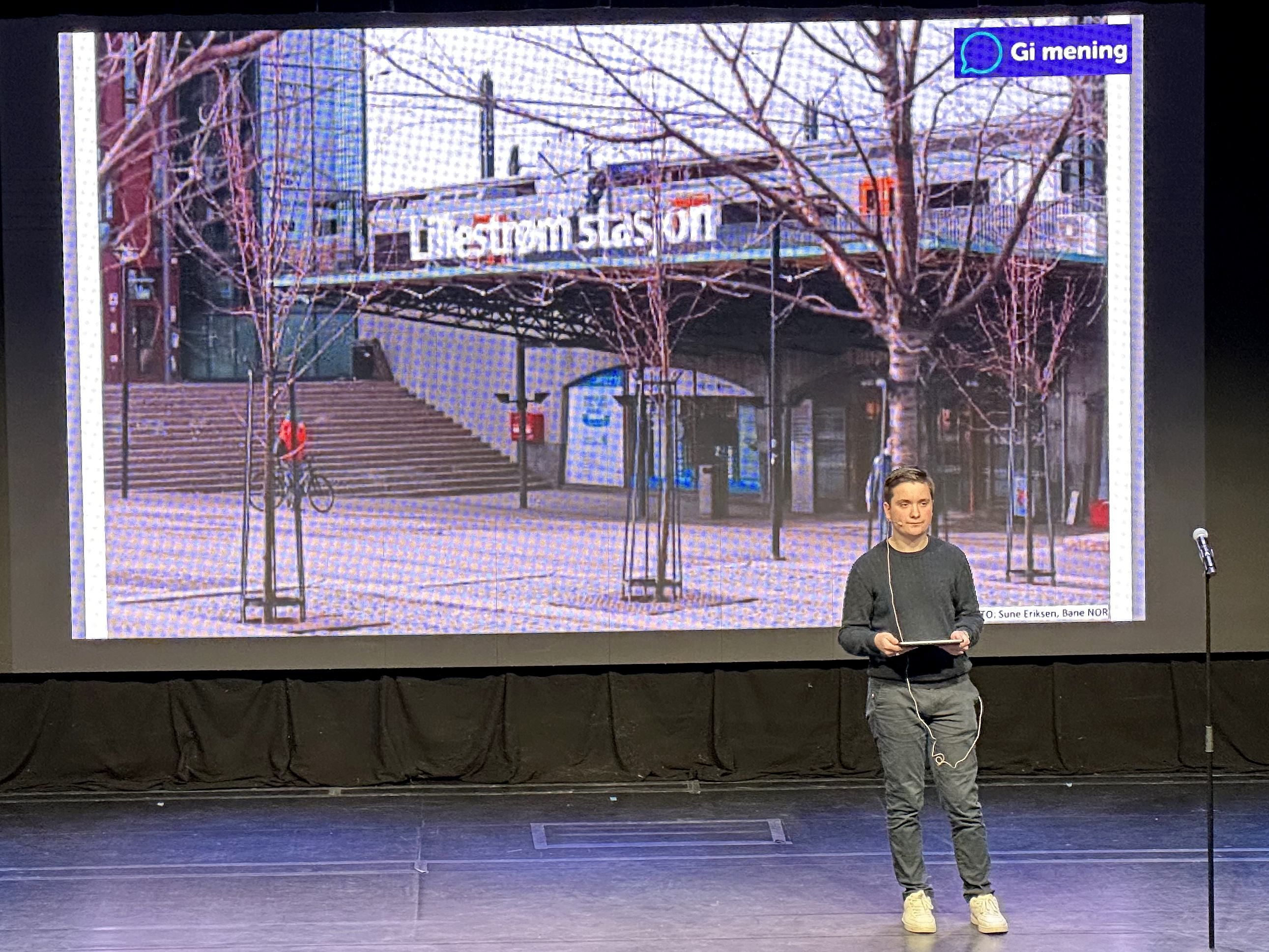 Bildet viser en ungdom på en scene. Bak ham er det et lerret, som viser bilde av Lillestrøm stasjon. 