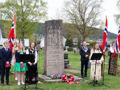Bildet viser totalt ti personer som står på hver side av en stor bauta. Fire av dem står med store norske flagg.