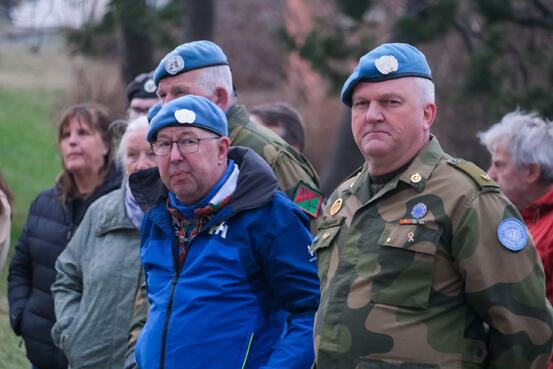 To menn ute. En har militær uniform og begge har blå beret. Mennesker i bakgrunn