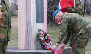 Mann i militær uniform legger ned en blomsterkrans ved et minnemonument.