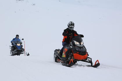 To snøskutere med førere som kjører i skuterløypa