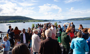 Bildet viser masse folk som går utpå brygga. Man ser Randsfjorden, åser og blå himmel i bakgrunnen.