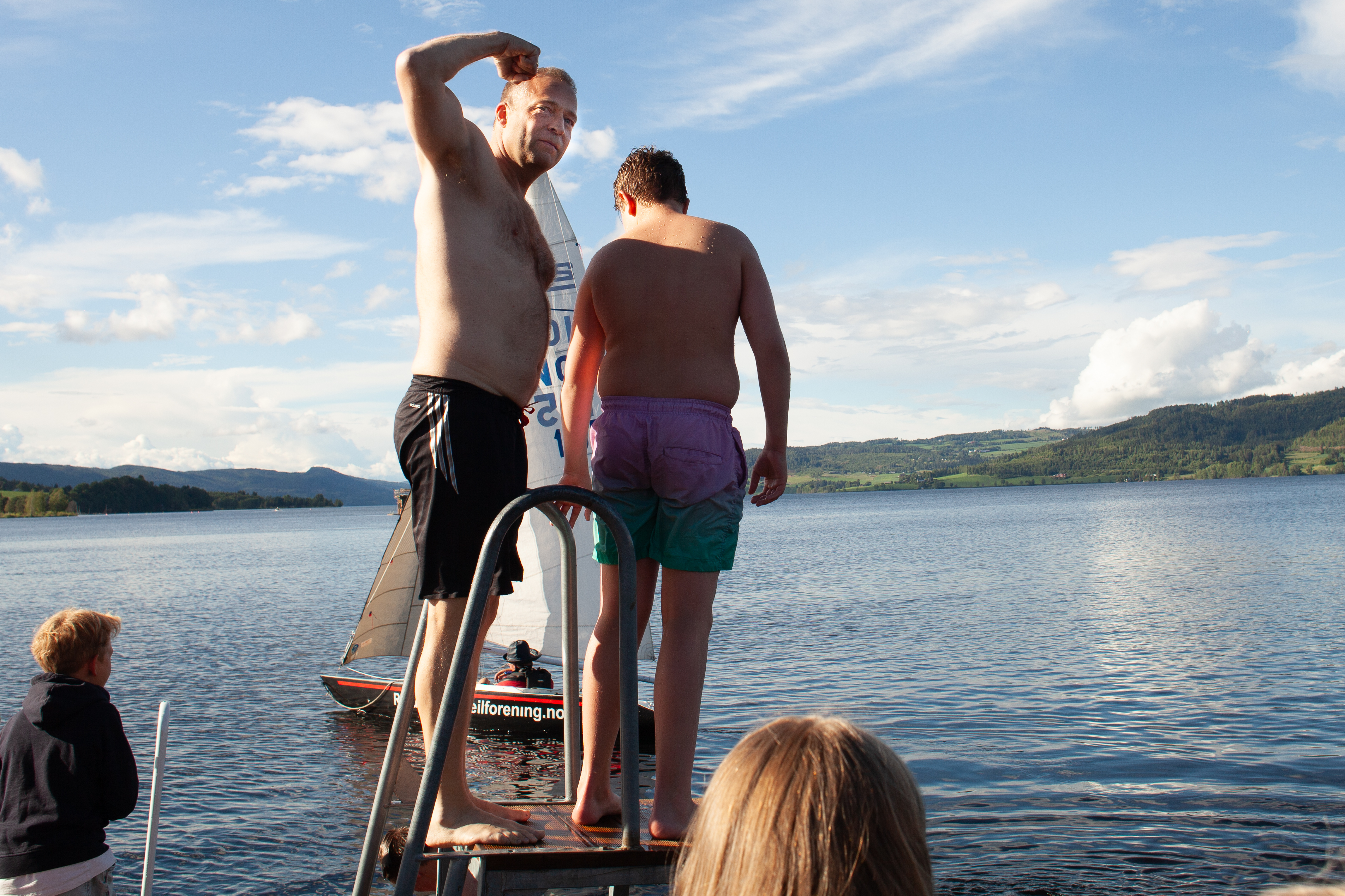 Bildet viser en mann i badebukse på toppen av et stupetårn. Han viser muskler.