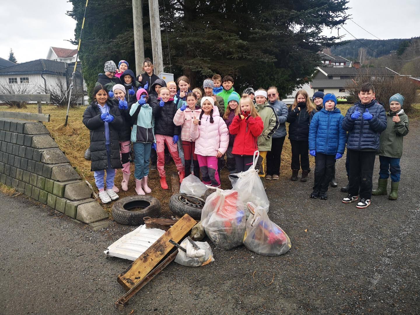 Bildet viser en elevgruppe som står bak en haug med avfall, både planker, dekk og plastposer fylt med mindre ting.