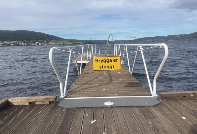 Bildet viser ei flytebrygge. Mellom rekkverkene et skilt hvor det står "Brygga er stengt".