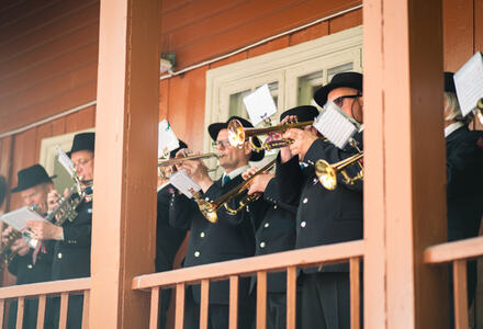 Musikanter som spiller trompet stående på en veranda. Foto. 