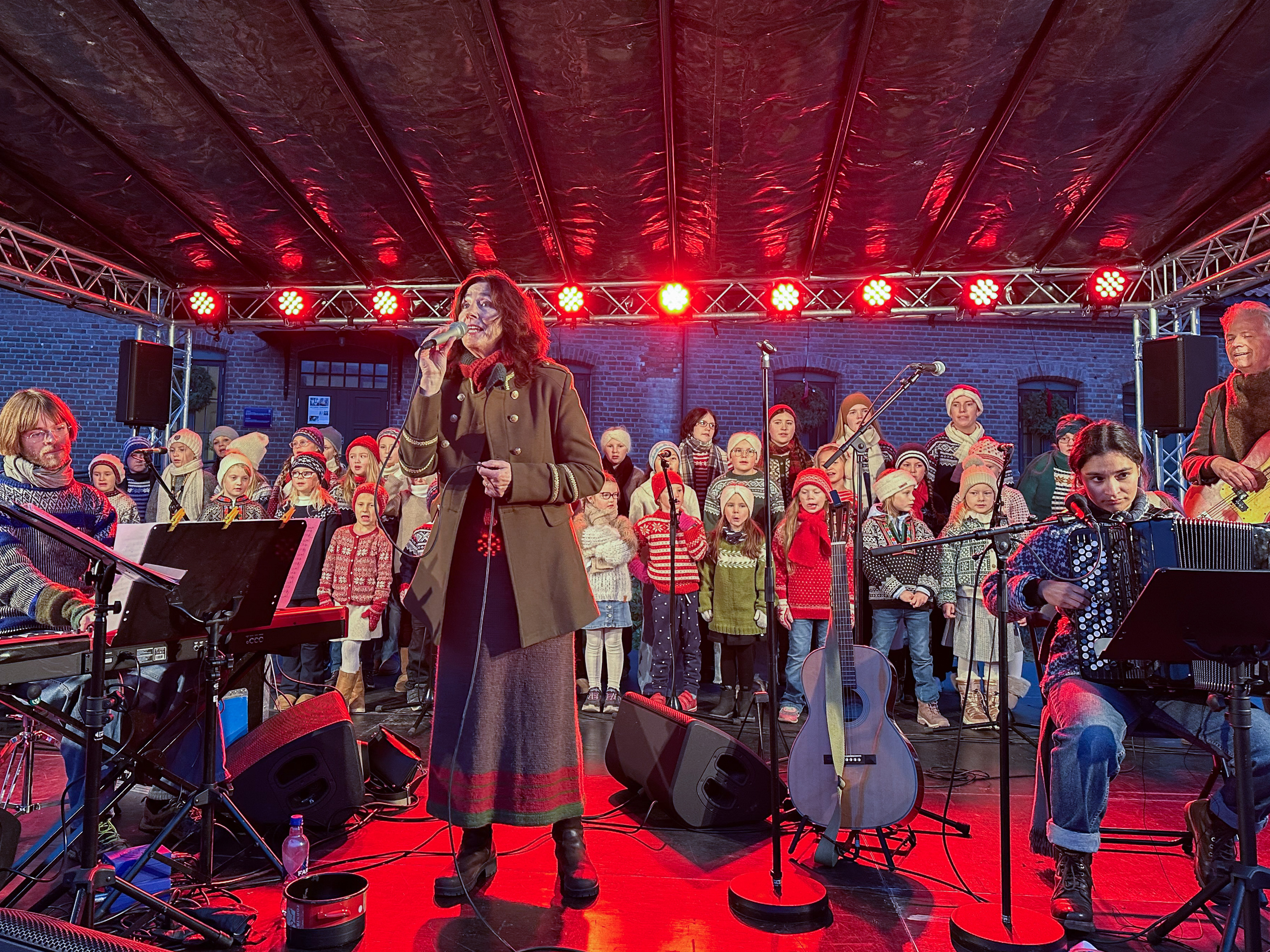 Bildet viser en artist (stående midt i bildet), hennes band og bak et barnekor.