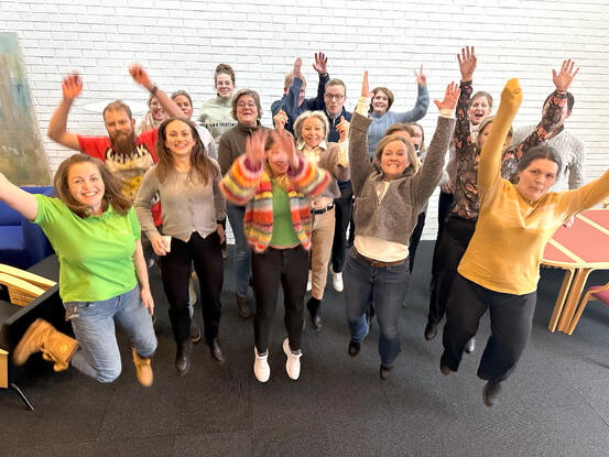 Bildet viser en stor gruppe personer som hopper med armene i været og store smil.