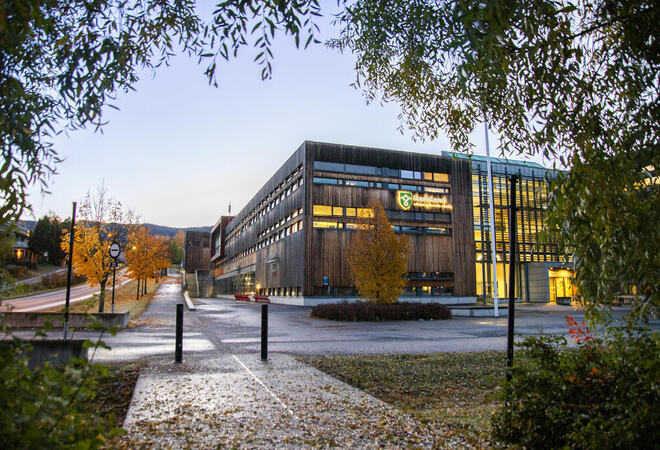 Bildet viser et stort bygg. Man kan se en logo på veggen med fylkesvåpenet til Innlandet fylkeskommune og teksten Hadeland videregående skole.