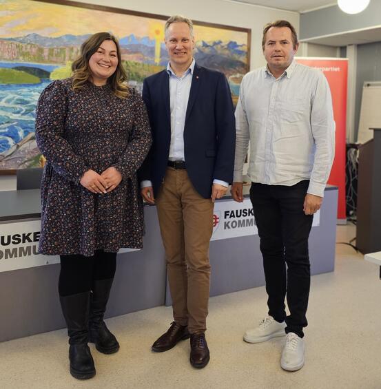 To menn og en kvinne står sammen og smiler