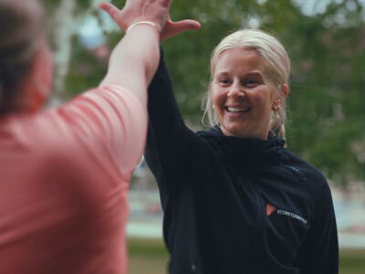 Bildet viser en person, som vi ser tydelig, som tar "High five" med en person som er uskarp, og som vi ser bare deler av, bakfra.