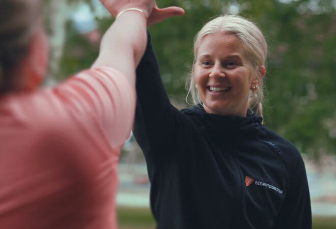 Bildet viser en person, som vi ser tydelig, som tar "High five" med en person som er uskarp, og som vi ser bare deler av, bakfra.