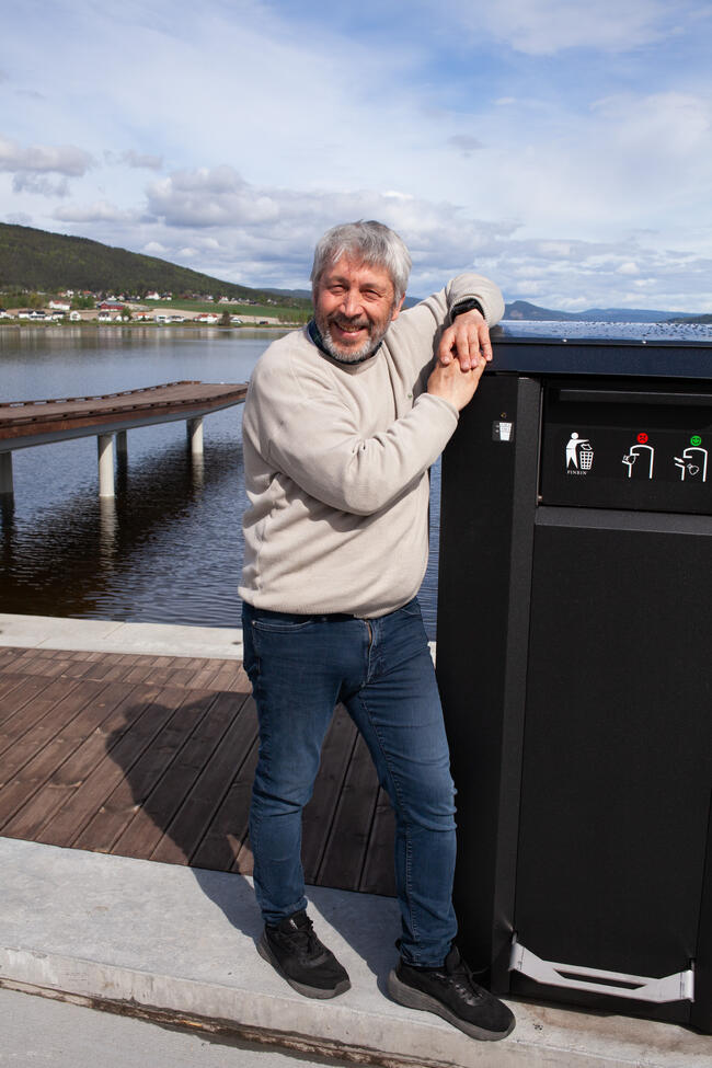 Bildet viser en person som står ved en høy avfallsdunk. Bak til venstre ser man den nye verkebrygga.