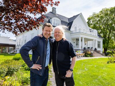 Bildet viser to storfornøyde personer som står ved siden av hverandre, med hendene opp på hverandres skulder. De står i en stor hage. Bak dem ser man en stor, ærverdig hvit bygning.