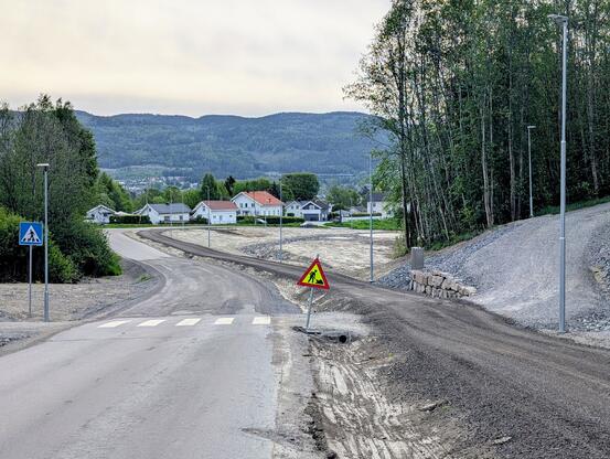 Bildet viser en bilvei med en gangvei ved siden av. Gangveien er en grusvei. Det står et veiarbeidsskilt i grøfta mellom veiene.