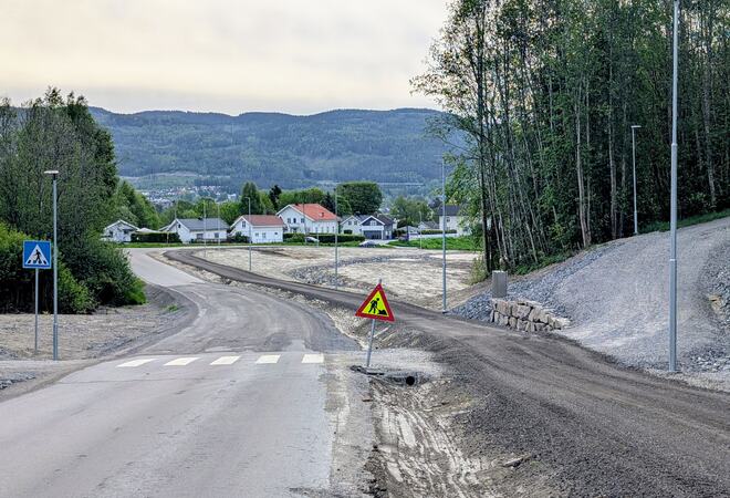 Bildet viser en bilvei med en gangvei ved siden av. Gangveien er en grusvei. Det står et veiarbeidsskilt i grøfta mellom veiene.