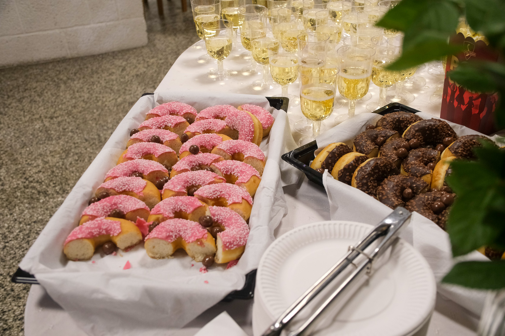 Rosa og brune donuts lagt i et fat på bord. Glass med bobler i bakgrunn
